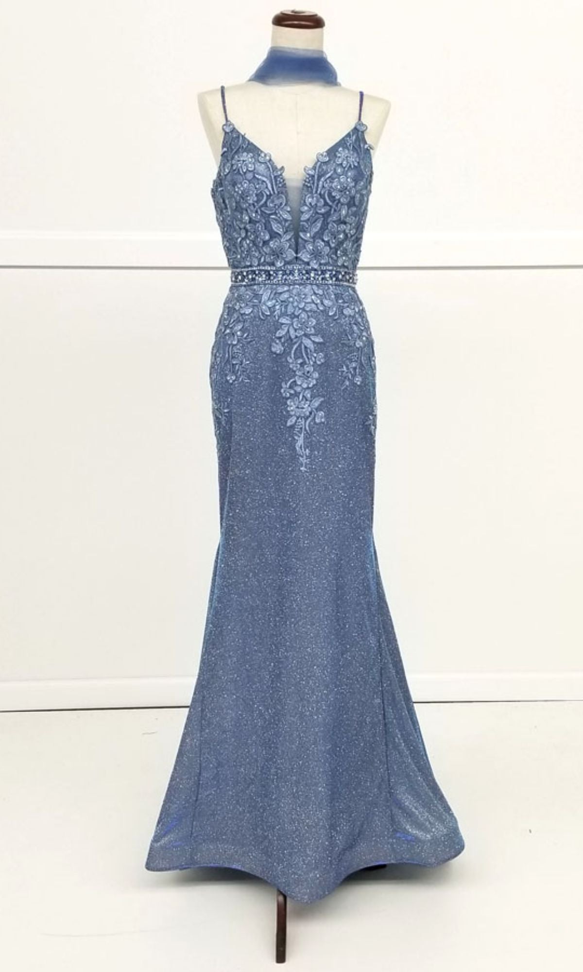 The Low-Back Long Mermaid Prom Dress: Chicas C243 is a sleeveless, floor-length blue gown with spaghetti straps, floral lace embroidery on the bodice, a beaded waistband, and a matching choker displayed on a dress form.